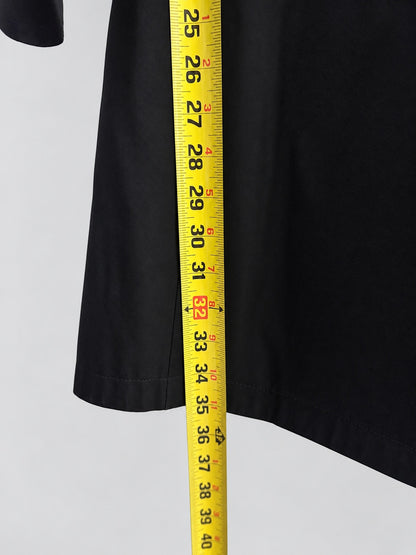 A close-up of a black garment sleeve or hem with a yellow measuring tape running vertically to show the length in inches and centimeters against a light gray background.