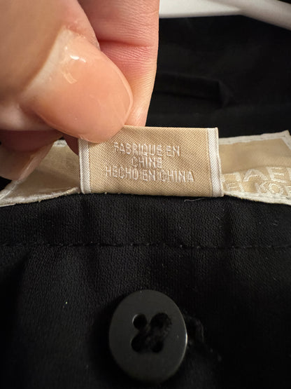 A close-up of a hand holding a beige fabric label sewn onto a black garment. The label reads 'FABRIQUE EN CHINE / HECHO EN CHINA' in gray text.