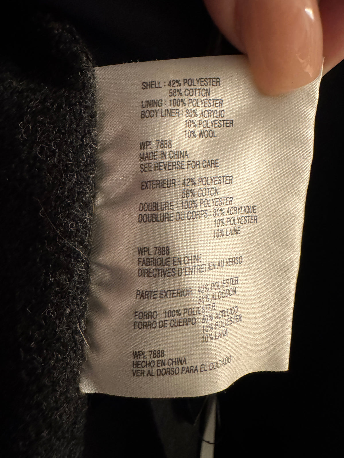 A close-up of a garment's interior care label held by a hand, showing fabric composition details in English and French.