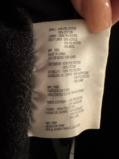 A close-up of a garment's interior care label held by a hand, showing fabric composition details in English and French.
