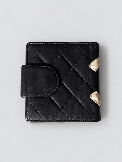 A black quilted leather wallet with a snap tab closure and two small gold-tone shield-shaped metal accents on the side, shown on a light gray background.