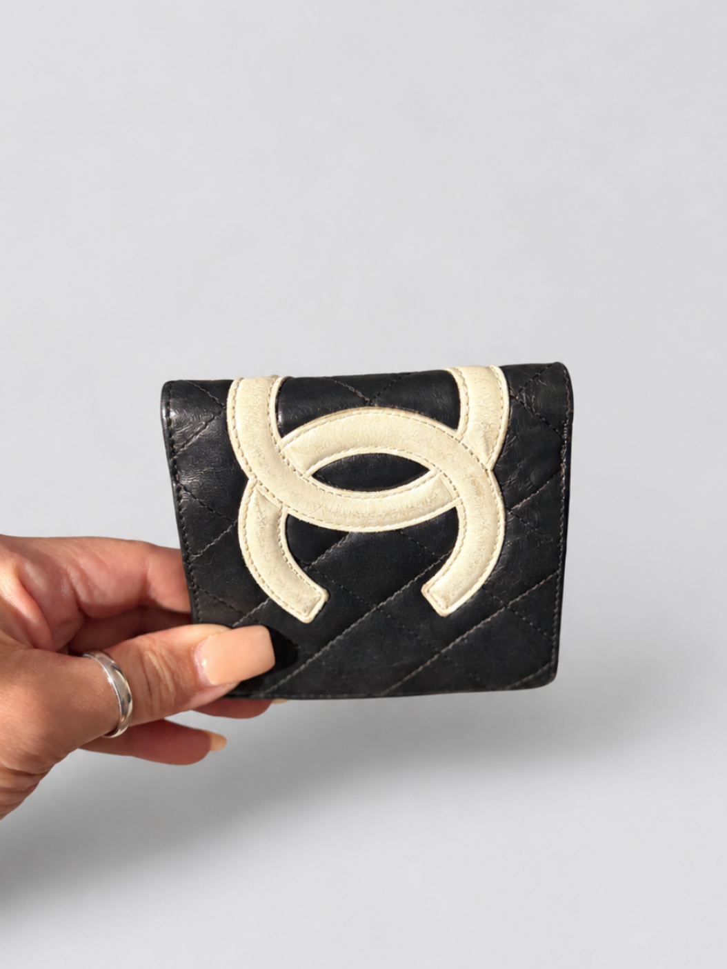 A hand holding a black quilted leather wallet featuring a large cream-colored interlocking CC logo on the front, set against a plain light gray background.