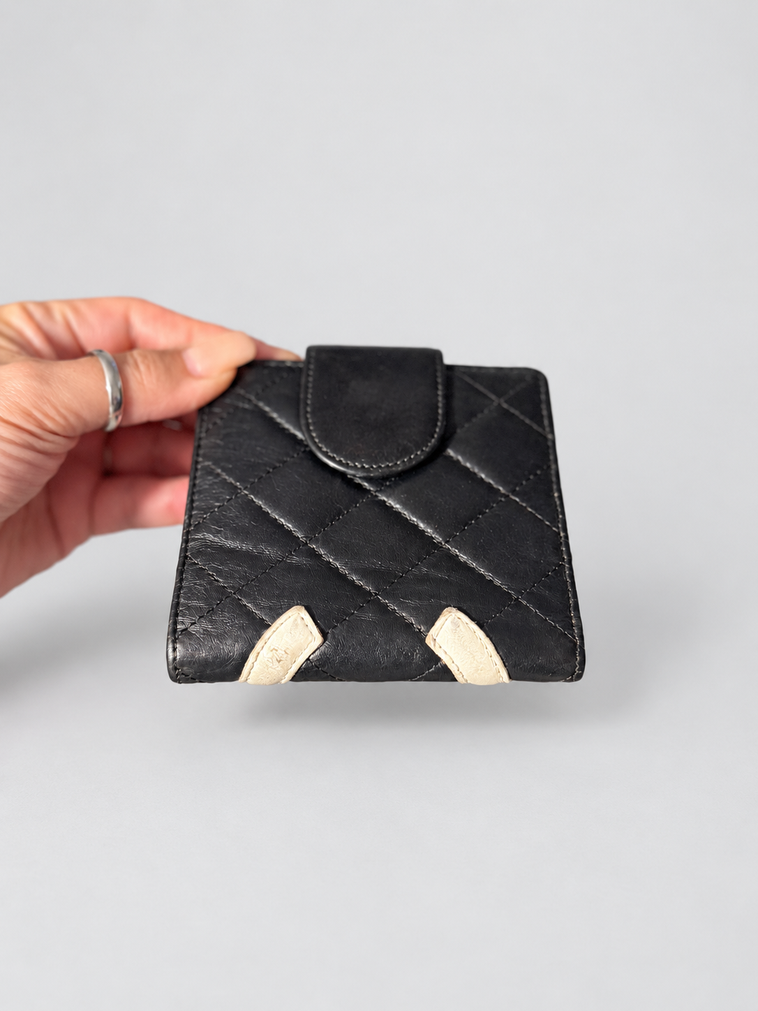 A hand holding a black quilted leather wallet with cream-colored corner accents against a plain light gray background.
