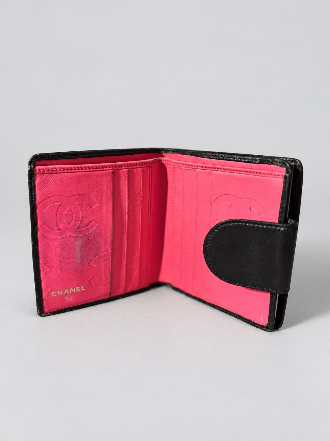 An open Chanel bi-fold wallet in black leather with a vibrant hot pink interior, featuring embossed Chanel logos and card slots.