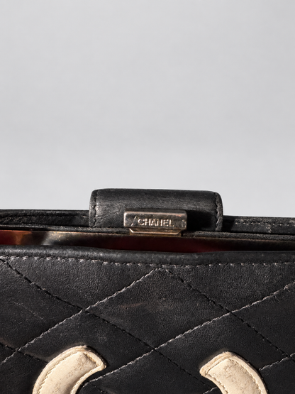 Close-up of a vintage Chanel clutch bag featuring a black leather body with diamond-quilted stitching, a tortoiseshell-patterned metal frame, and a silver-tone metal clasp engraved with the CHANEL brand name.