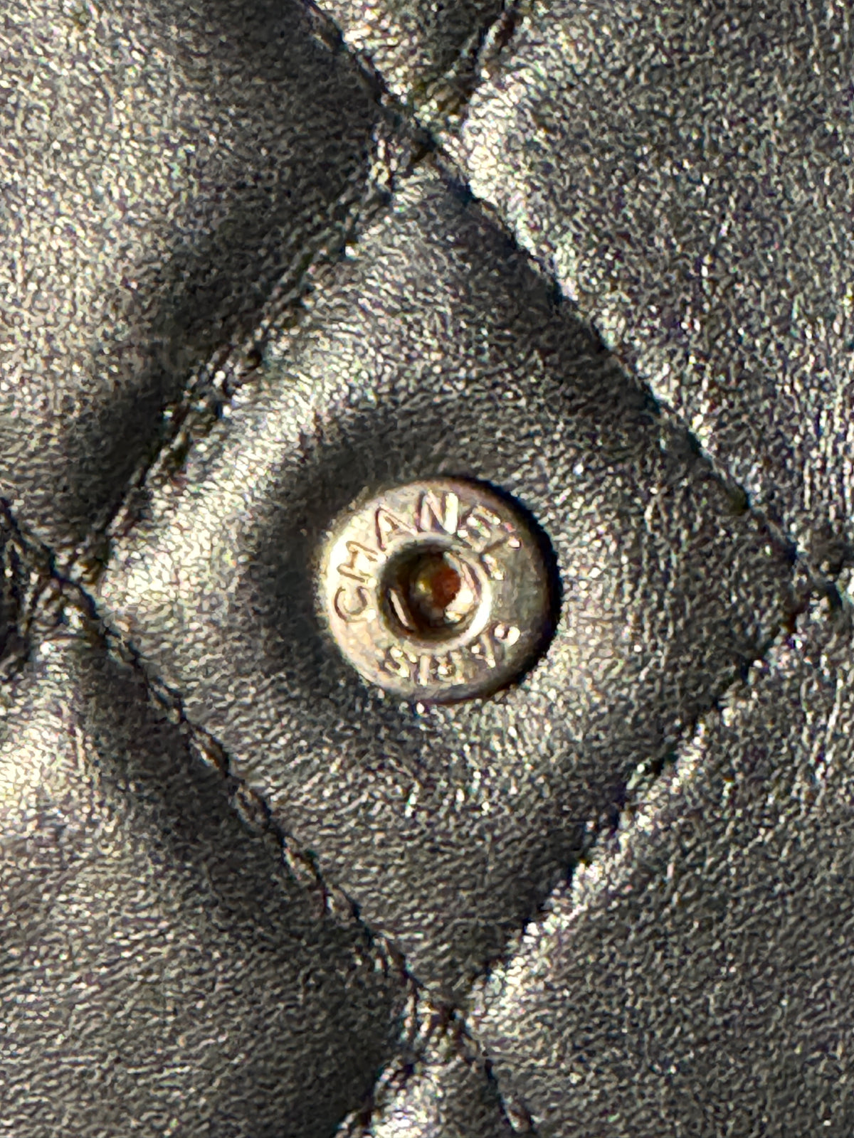 Close-up of a quilted black leather jacket with a silver-tone Chanel snap button.