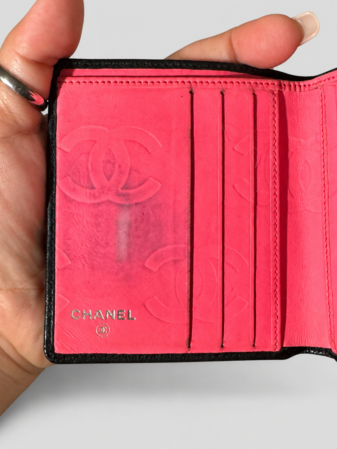 A close-up of a Chanel bi-fold wallet held in a hand, showing the interior in bright pink with embossed Chanel logo and the CHANEL name printed near the bottom.