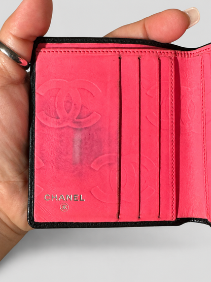 A close-up of a Chanel bi-fold wallet held in a hand, showing the interior in bright pink with embossed Chanel logo and the CHANEL name printed near the bottom.