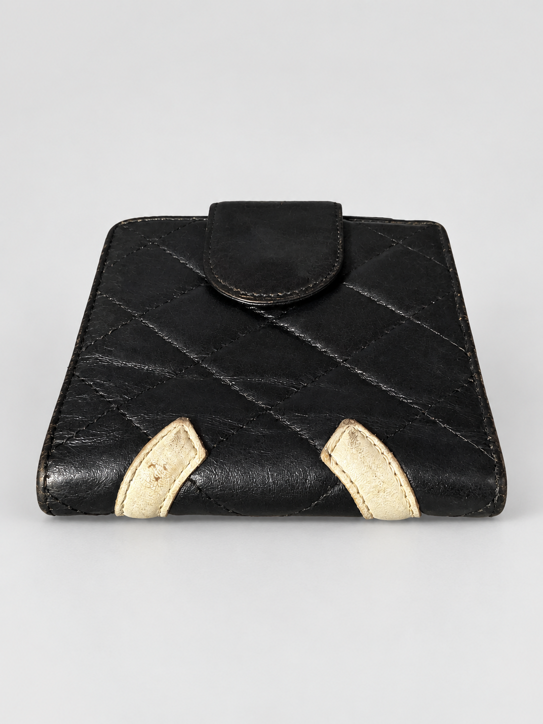A black quilted leather wallet with two contrasting beige leather tab accents at the bottom corners, shown against a neutral light gray background.