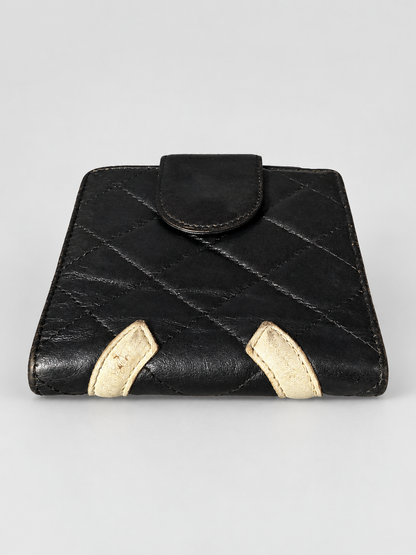 A black quilted leather wallet with two contrasting beige leather tab accents at the bottom corners, shown against a neutral light gray background.