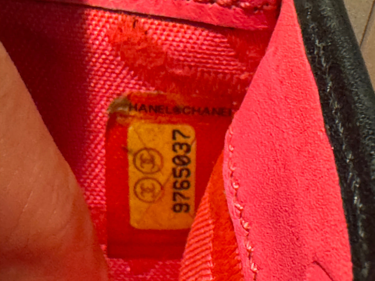 Close-up of the interior lining of a bright pink Chanel handbag, showing a yellow size tag with Chanel branding and a black serial number.