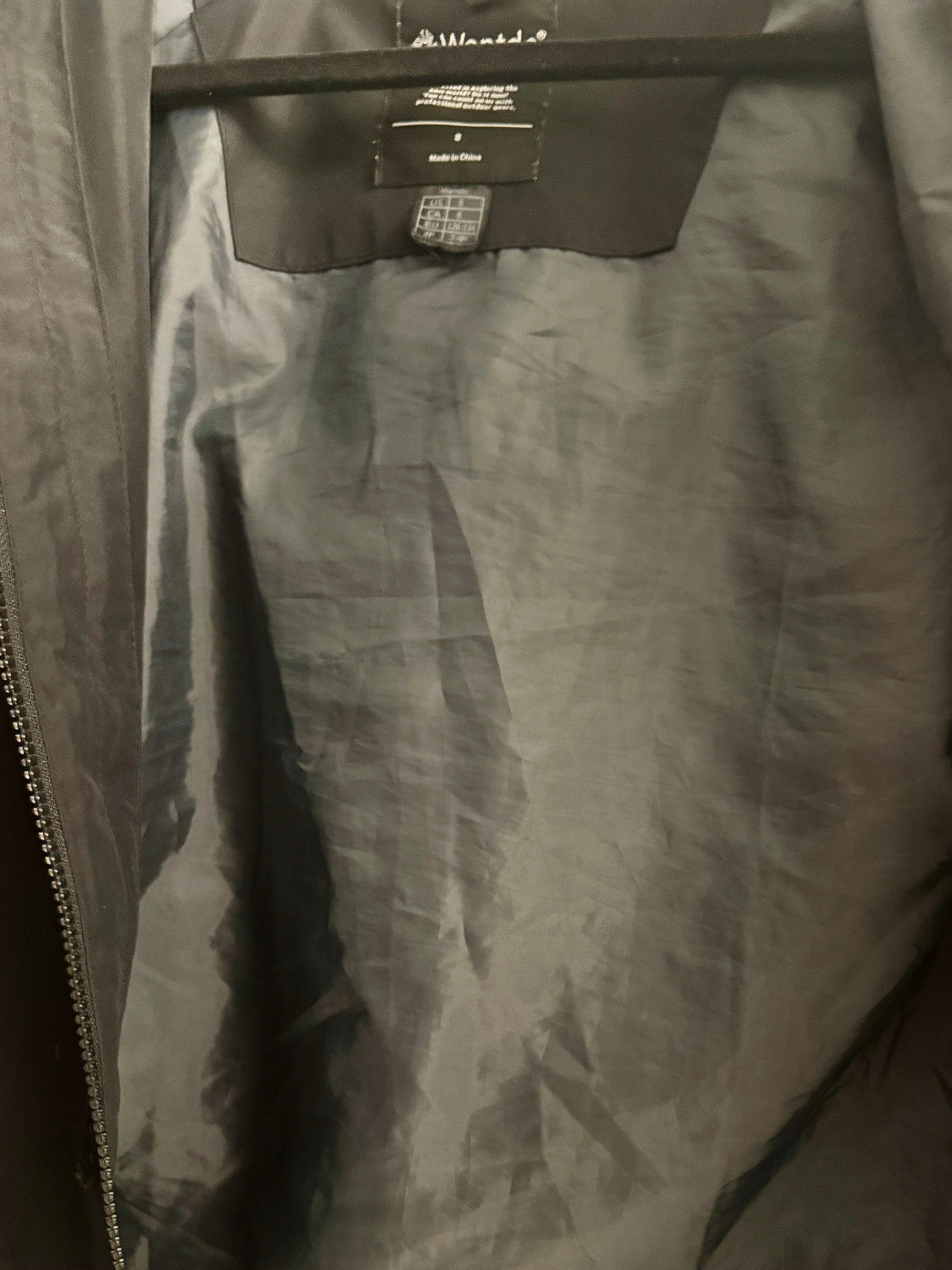 Close-up of the interior of a dark gray zippered jacket or coat, showing the inner lining, zipper track, and a hangtag near the collar.