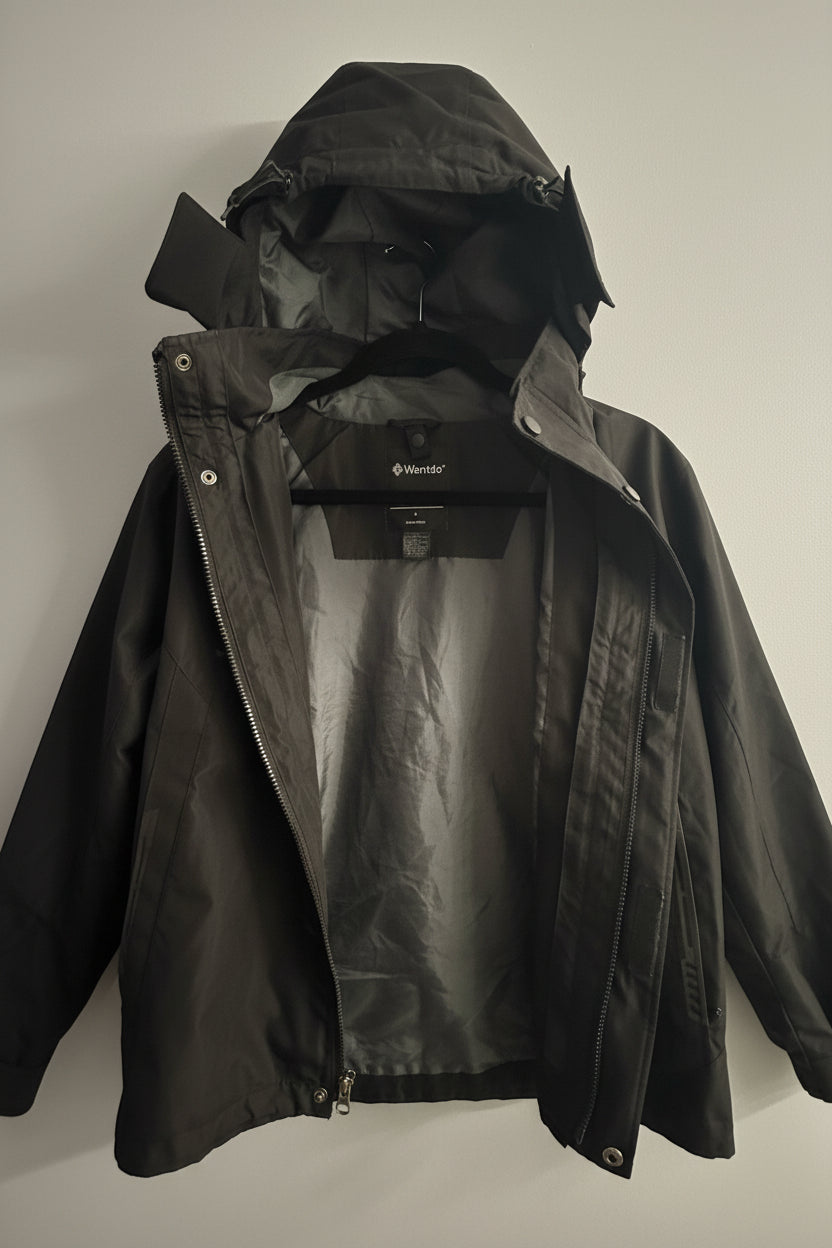 A black waterproof hooded jacket hanging on a hanger against a white paneled door. The brand name 'Munich' is visible on the inner neck label.