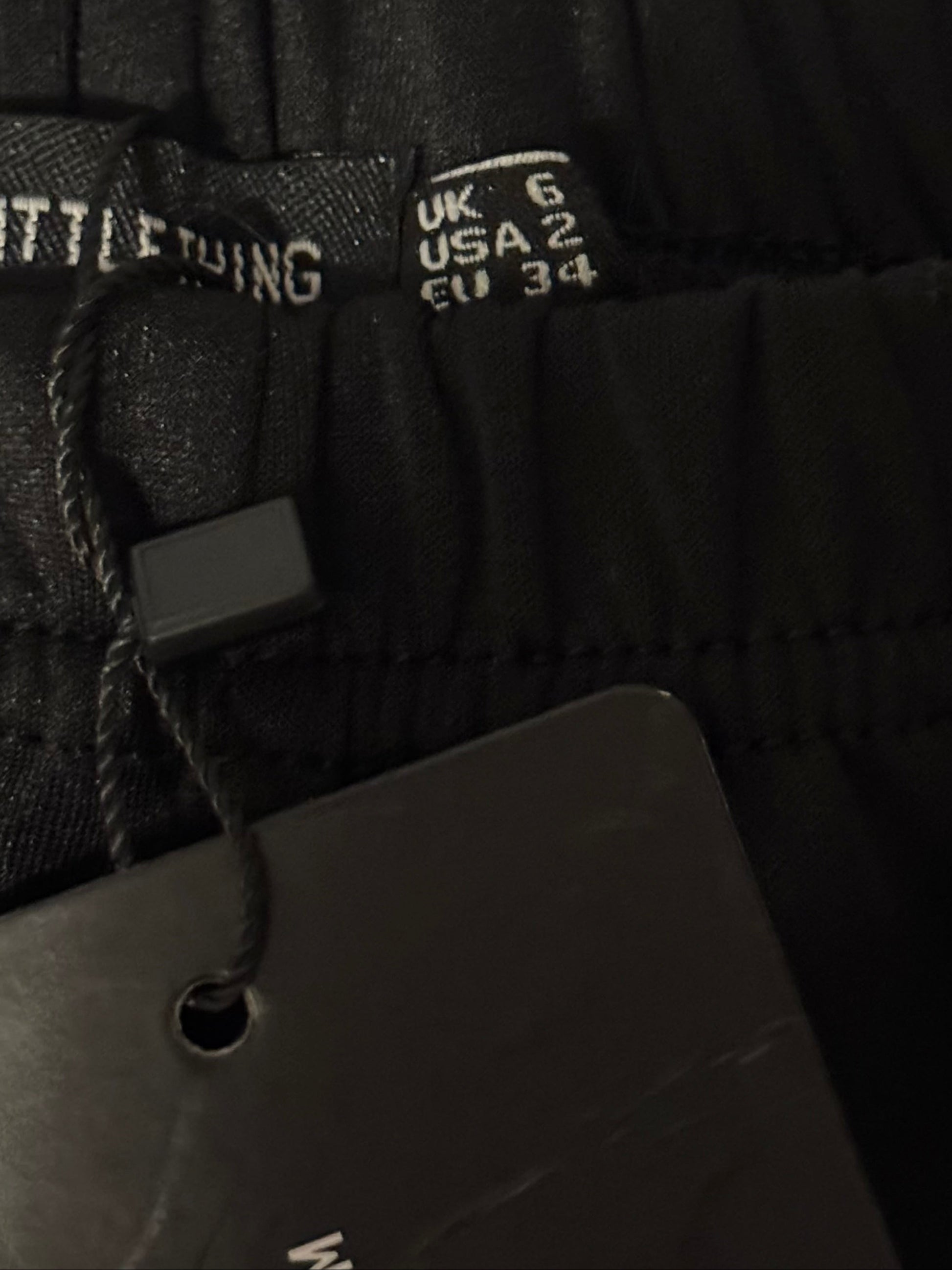 Close-up of black pants with size tags on a textured surface