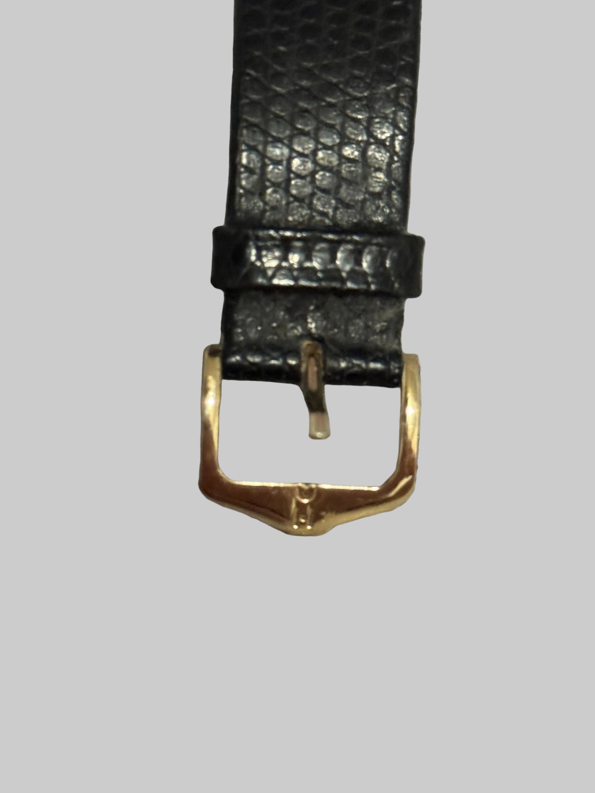 Black textured watch strap with gold buckle on a gray textured surface