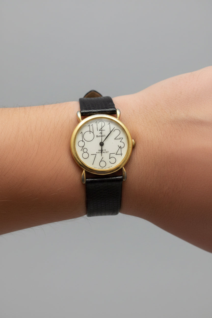 Wrist wearing a watch with a black strap and gold case on a textured surface.