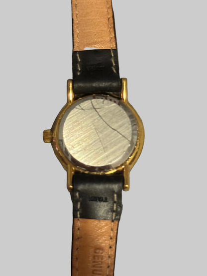 Worn wristwatch with a gold case and black leather strap on a textured gray background