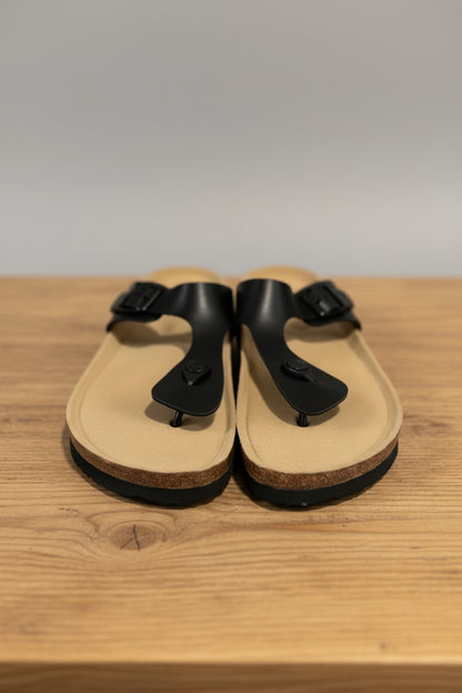 Pair of tan sandals with black straps on a textured surface