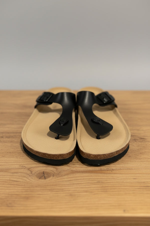 Pair of tan sandals with black straps on a textured surface