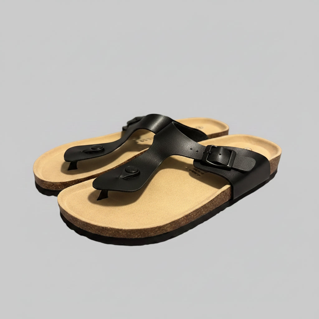 Pair of black sandals with tan soles on a textured surface