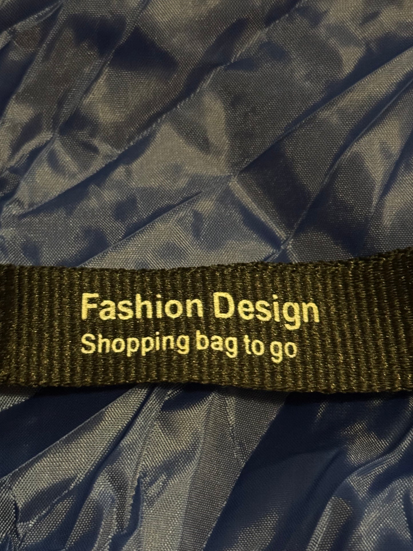 Black shopping bag with a green strap labeled 'Fashion Design Shopping bag to go' on a black background