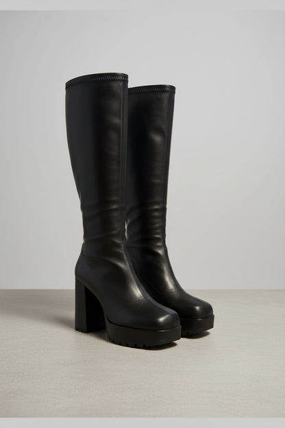 Pair of black leather boots on a carpeted floor with a blurred background