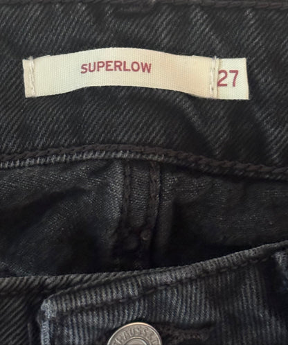 Close-up of a jeans label with 'Superlow' and size '27' on a dark denim background.