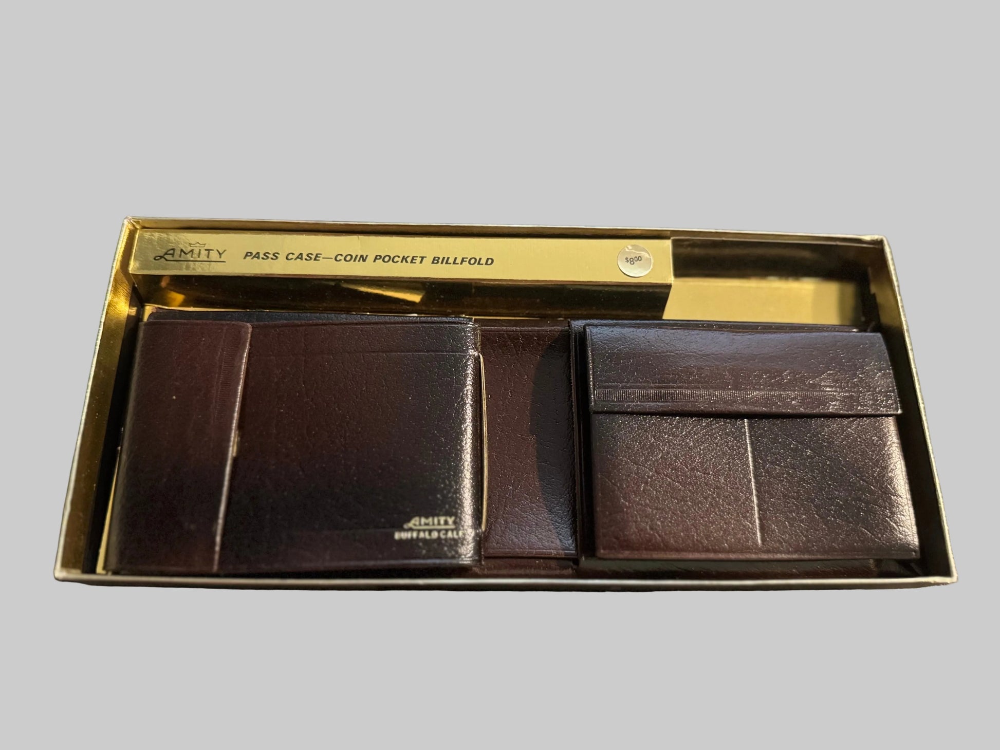 Set of leather wallets in a box with 'Amity' branding on a textured surface.