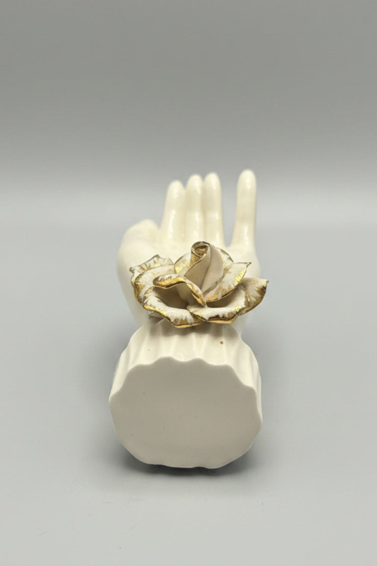 A white ceramic hand-shaped ring holder with a gold-tone ring on its fingers, displayed on a dark wood tabletop.
