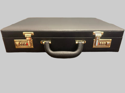 A black faux-leather briefcase with gold-tone hardware, including combination dials and a central handle, resting on a wooden table.