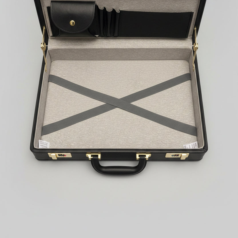 An open black leather briefcase or travel case with a gray textured interior lining, gold-tone hardware, and a white envelope or document placed inside.