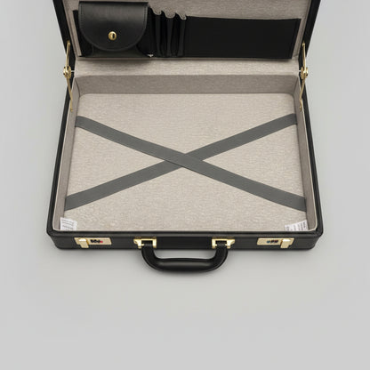 An open black leather briefcase or travel case with a gray textured interior lining, gold-tone hardware, and a white envelope or document placed inside.