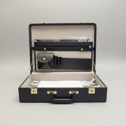 A black leather accessory organizer case shown open, revealing a beige interior organizer with black straps, a small black pouch with a gold snap, and a white paper insert at the bottom.