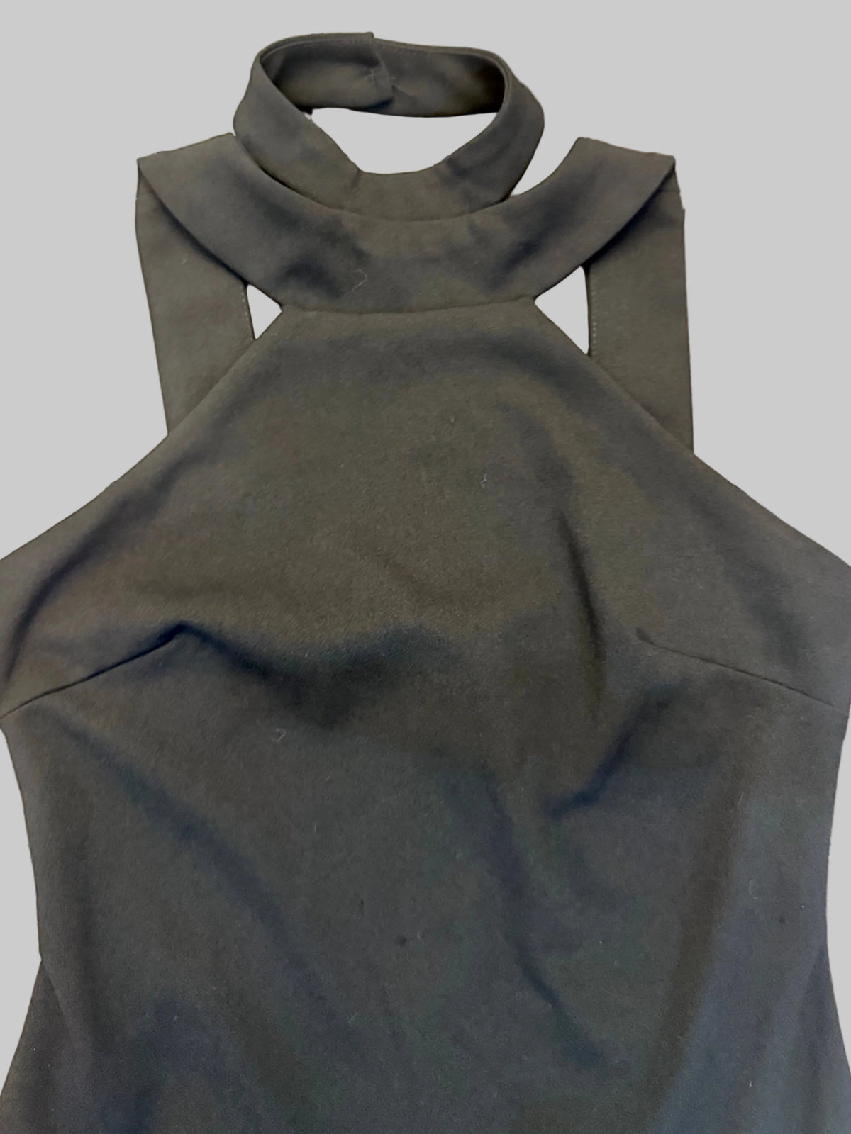 A black sleeveless halter-neck top with a wide collar and shoulder cutouts, laid flat on a brown wooden plank floor.