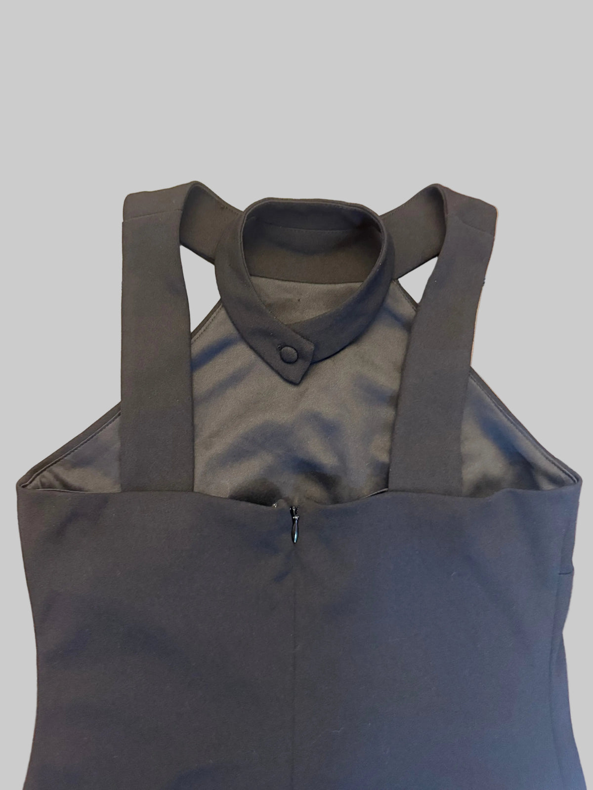 A dark gray sleeveless top with a mock collar and wide shoulder straps, laid flat on a wooden floor.