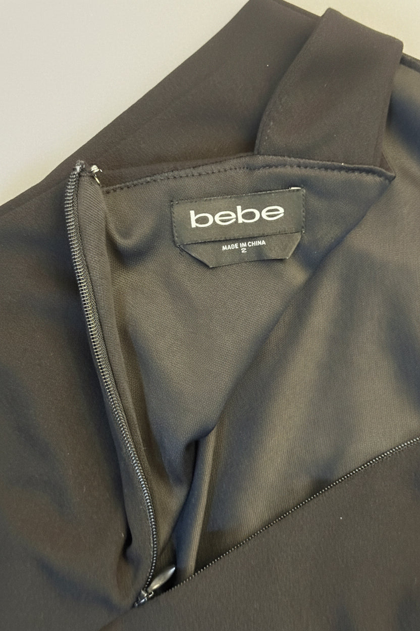Close-up of a black zippered garment with a visible 'bebe' brand label inside the collar, photographed on a wooden surface.