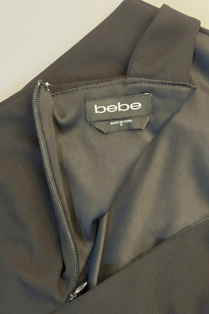 Close-up of a black zippered garment with a visible 'bebe' brand label inside the collar, photographed on a wooden surface.