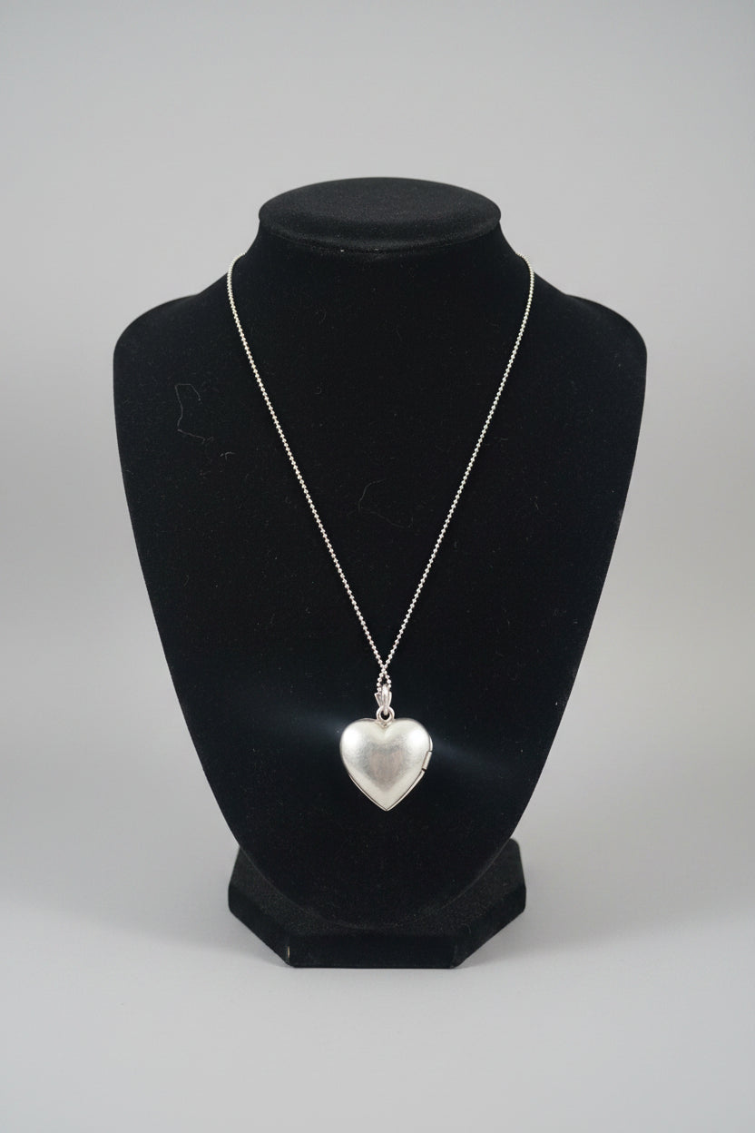 A silver heart-shaped pendant necklace displayed on a black jewelry bust over a wooden surface.