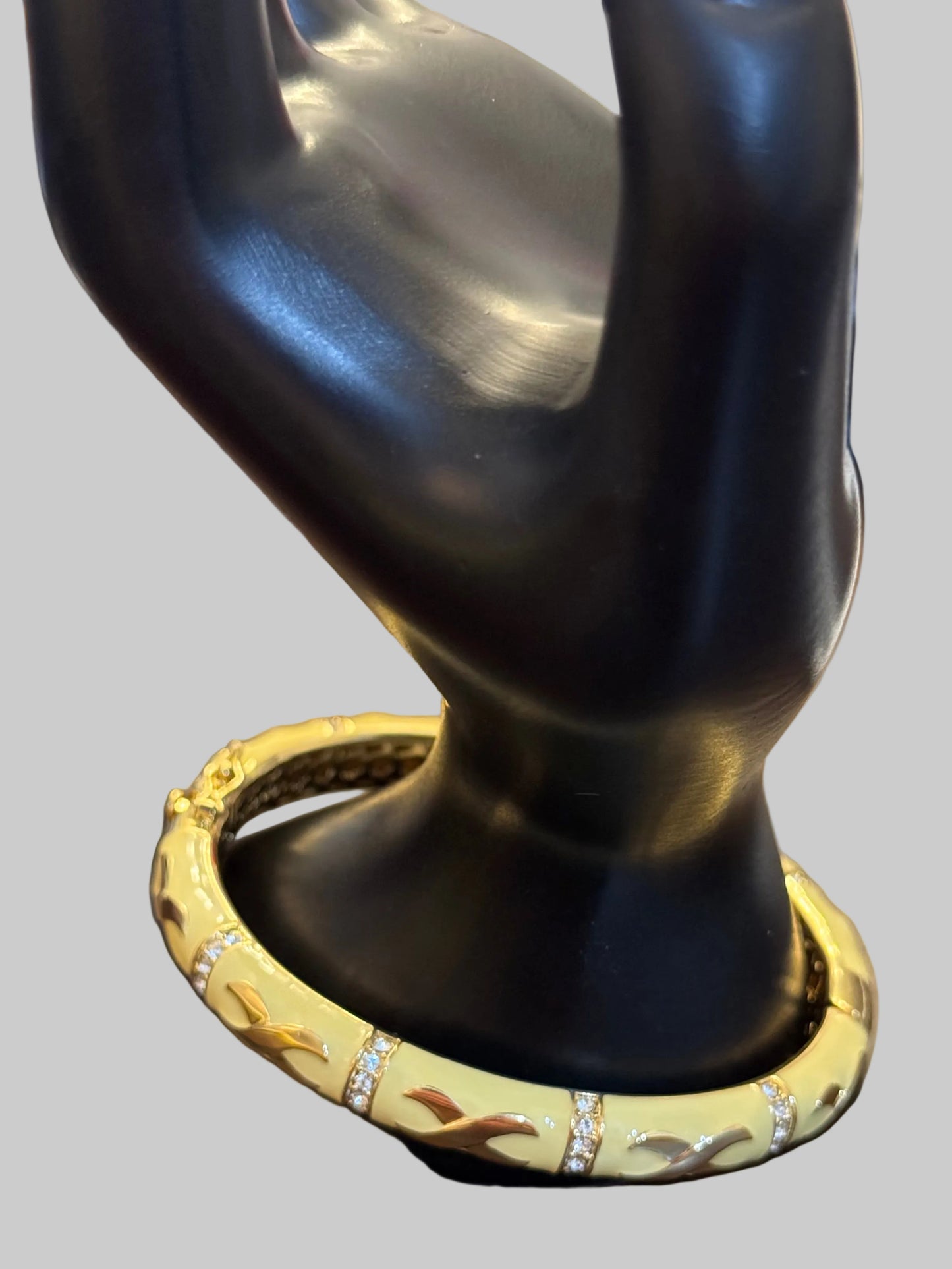 A gold bangle bracelet with a textured pattern and small clear stone accents, displayed on a black jewelry stand over a wooden table.