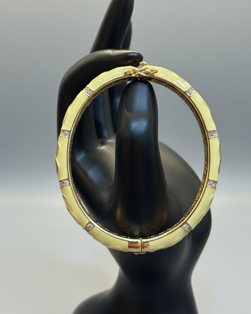 A gold-toned huggie bangle bracelet with pale yellow-green enamel segments and small clear rhinestone accents, displayed on a black jewelry stand.
