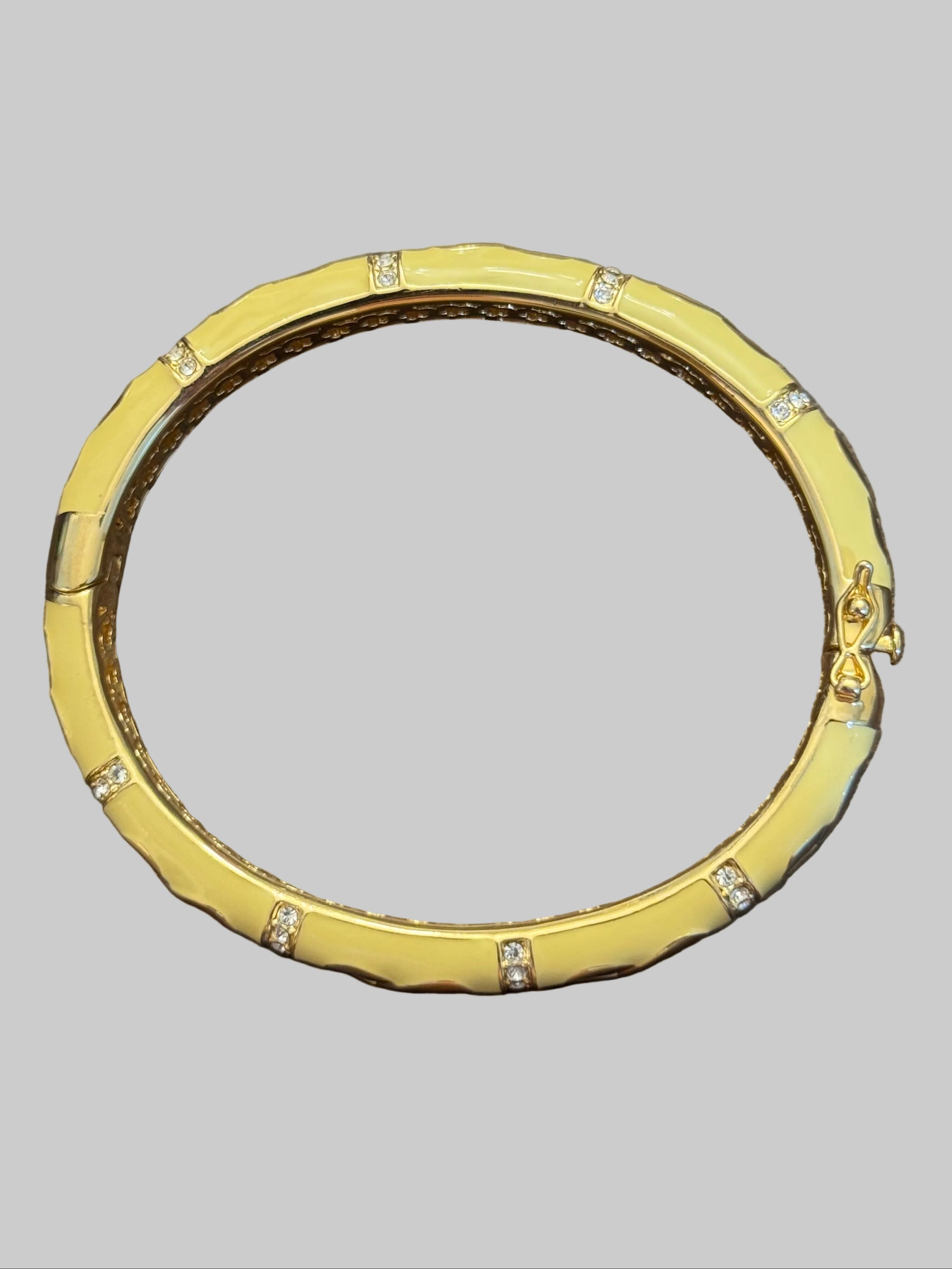 A gold bangle bracelet with a textured, segmented design and small clear crystal accents, displayed on a dark wooden surface.