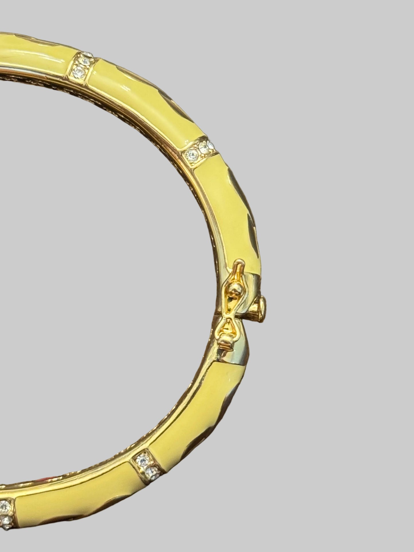 A close-up of a gold bangle bracelet with a textured segmented design and small clear crystal accents, resting on a dark brown wooden surface.
