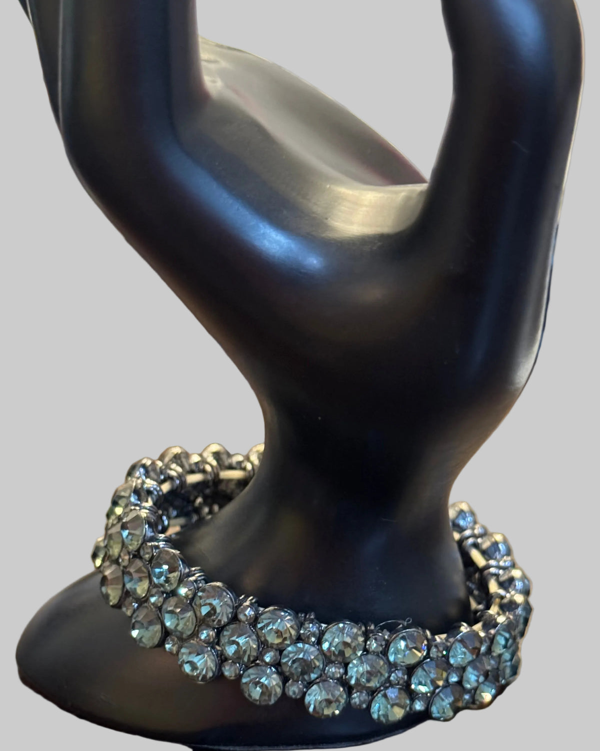 A close-up of a black display stand holding a silver-toned rhinestone-embellished ring or bracelet, set against a wooden surface.
