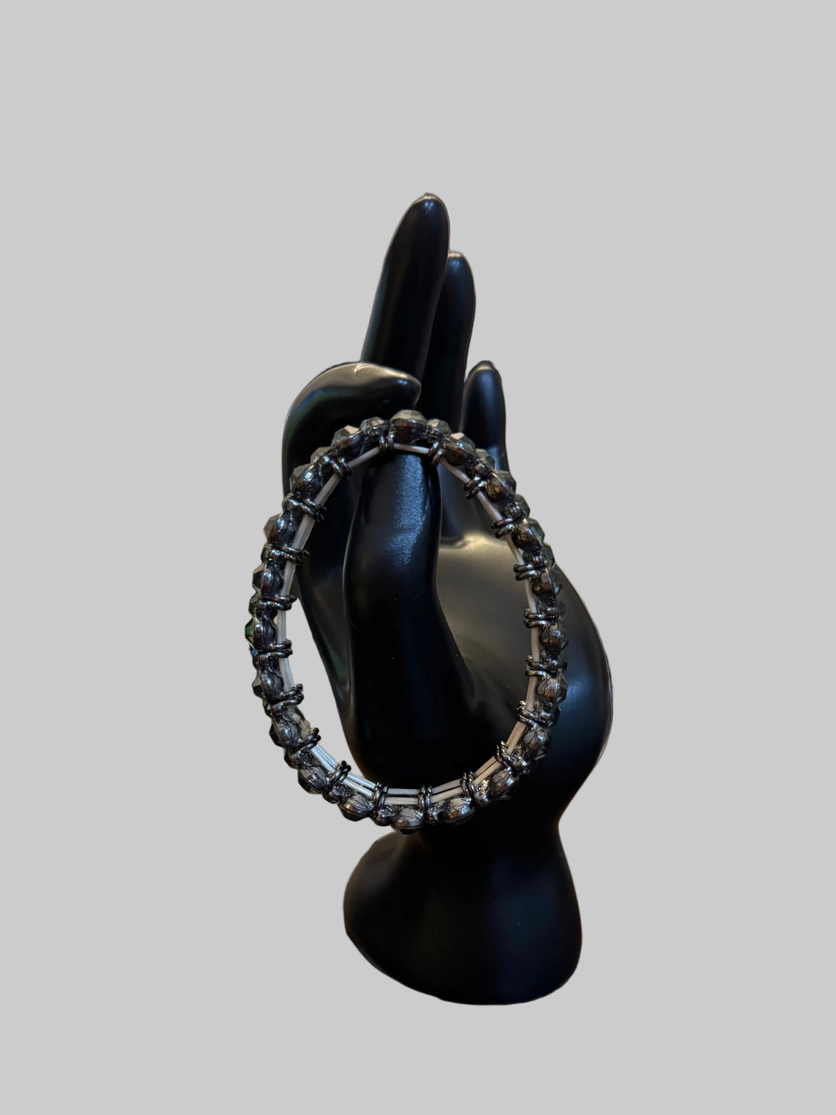 A silver-toned chain-link ring displayed on a black mannequin hand, set on a wooden table with a blurred jewelry store background.