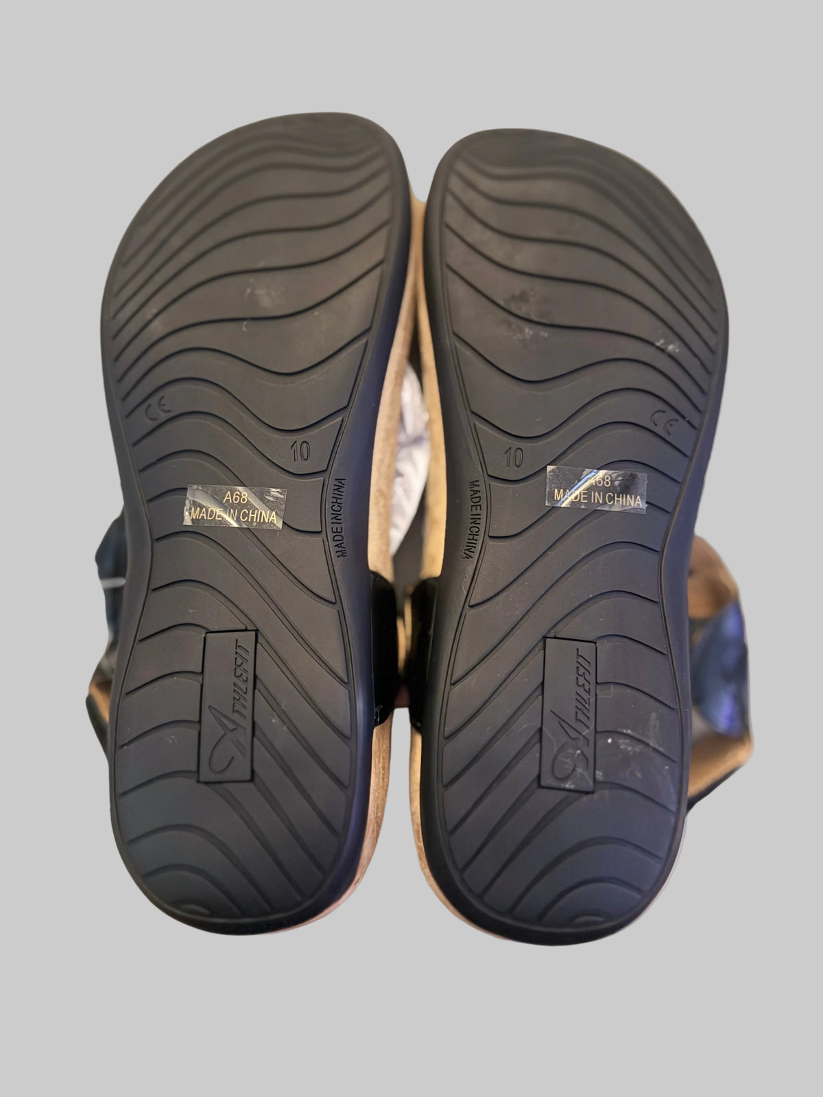 A pair of black Tassaron shoes shown from the sole view, resting on a light-colored wooden surface.