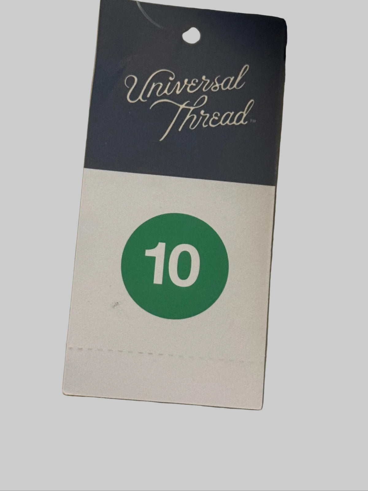 A Universal Thread size 10 garment tag attached to a sewing thread spool, resting on a neutral surface.