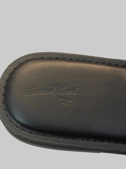 Close-up of a black leather shoe or boot sole with visible stitching and an embossed 'Universal Thread' logo, photographed on a light neutral surface.