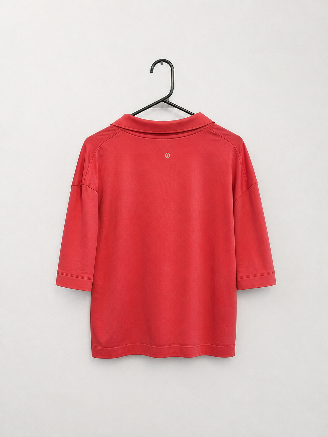 A red long-sleeve polo shirt hanging on a black metal hanger against a plain light gray wall.
