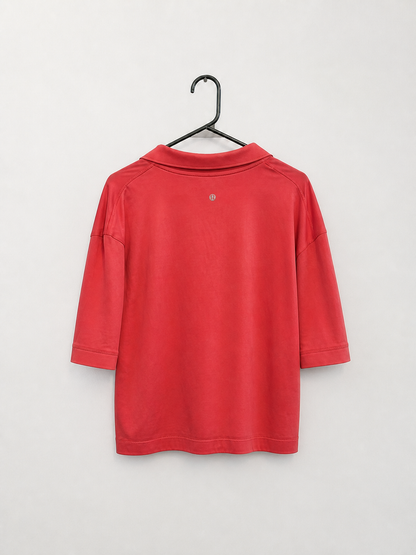A red long-sleeve polo shirt hanging on a black metal hanger against a plain light gray wall.
