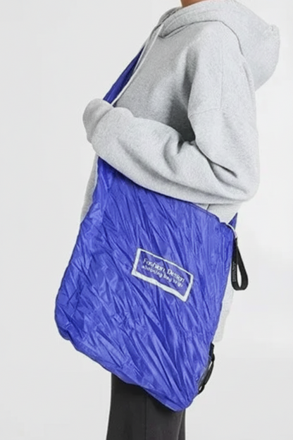 Person wearing a gray hoodie and blue quilted bag on a white background